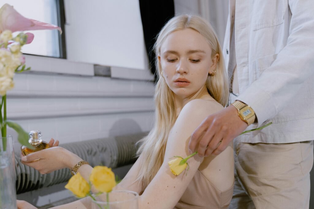 A woman sitting and a person putting a yellow flower next to her shoulder